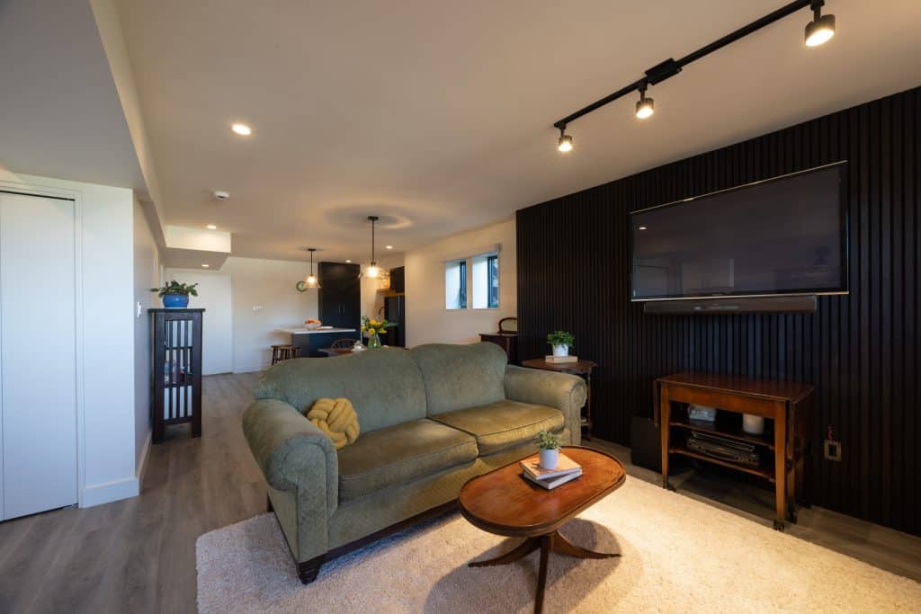 Modern basement living area featuring a green sofa, wooden coffee table, and wall-mounted TV, showcasing ReCraft Home Remodeling's design expertise in Portland.
