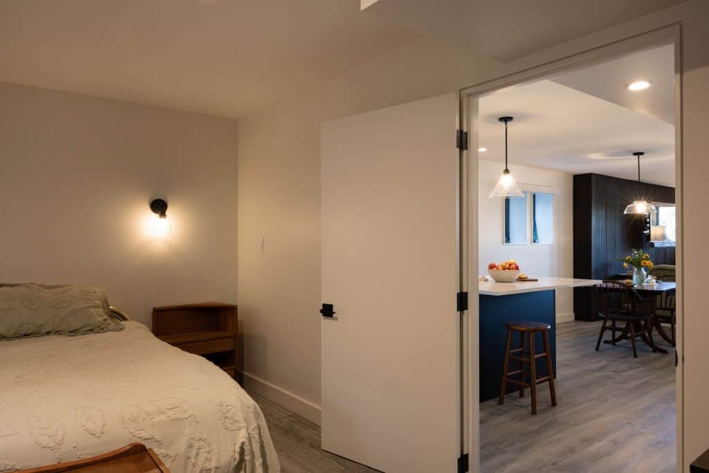 Cozy basement bedroom with modern decor, featuring a bed and a view of a stylish kitchen area, showcasing ReCraft Home Remodeling's renovation work in Portland.