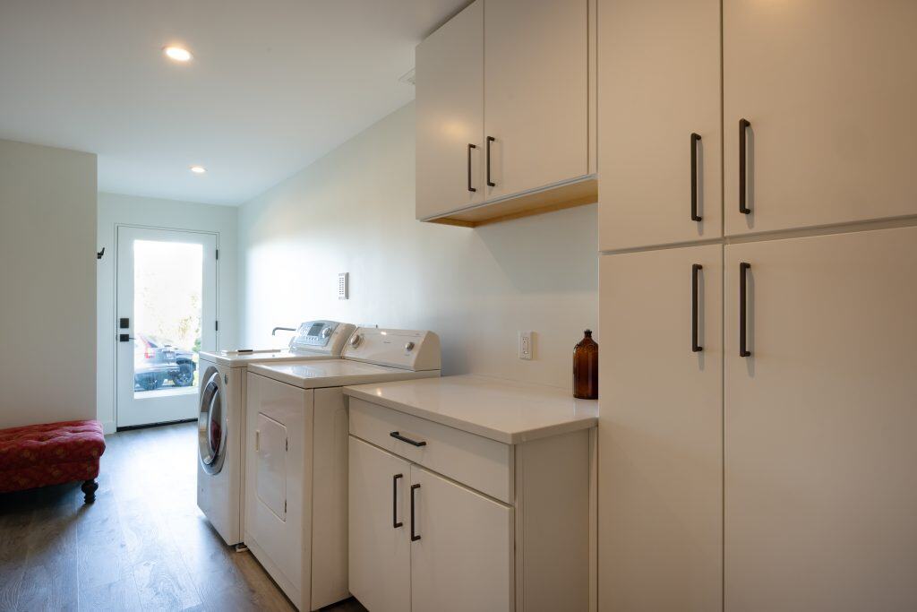 Modern basement laundry area featuring white cabinetry, washer and dryer, and natural light from a nearby door, showcasing ReCraft Home Remodeling's design expertise in Portland.