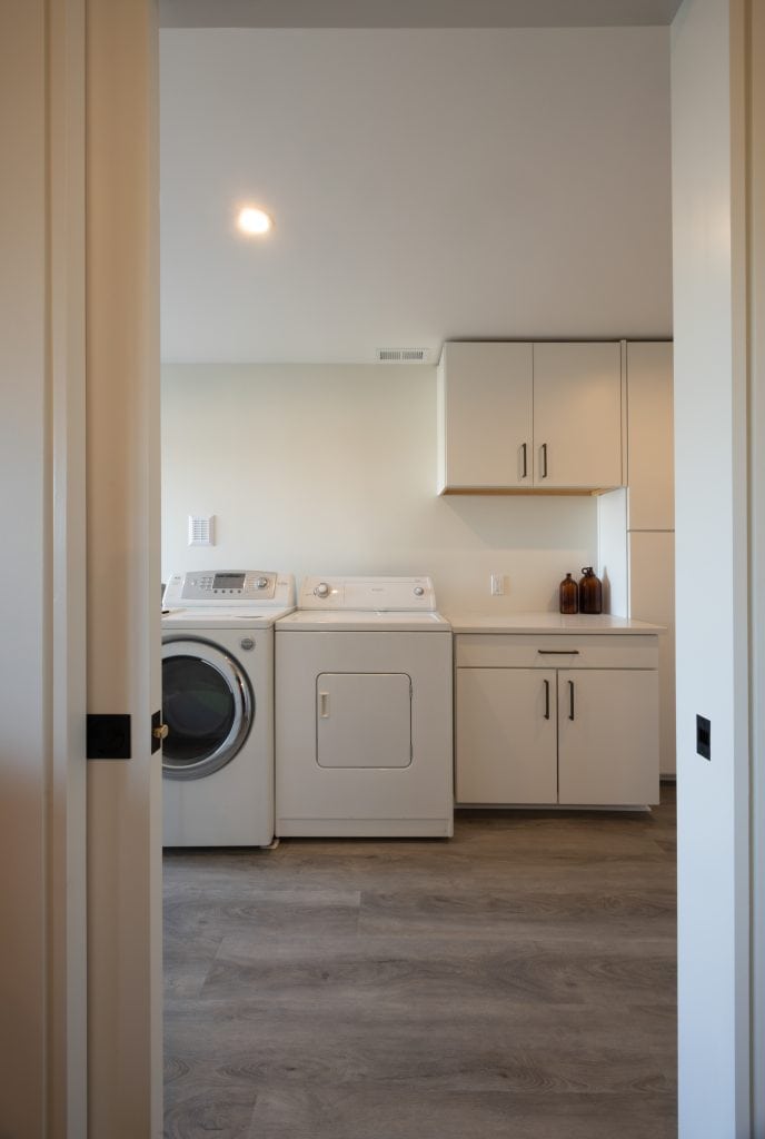 Laundry room with washer and dryer, modern cabinetry, and neutral-colored walls, showcasing a renovated basement space by ReCraft Home Remodeling in Portland.