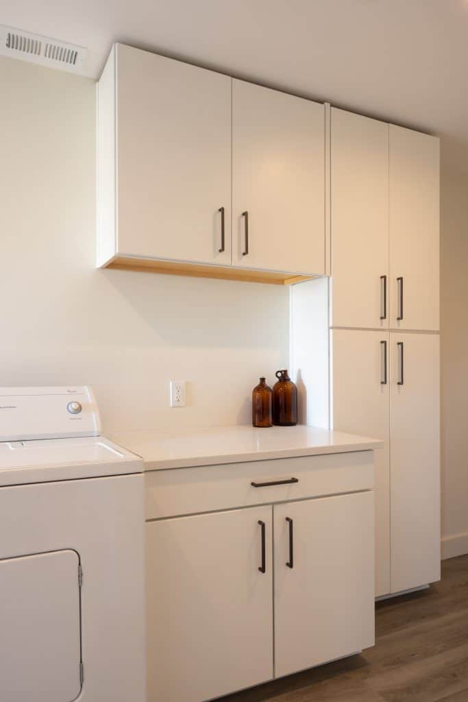 Modern basement laundry area with white cabinetry, washer, and decorative brown bottles, showcasing ReCraft Home Remodeling's renovation style.