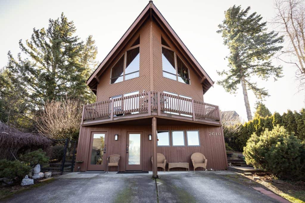 Brown two-story house with large windows, balcony, and landscaped yard, showcasing a potential basement remodeling project by ReCraft Home Remodeling in Portland, Oregon.