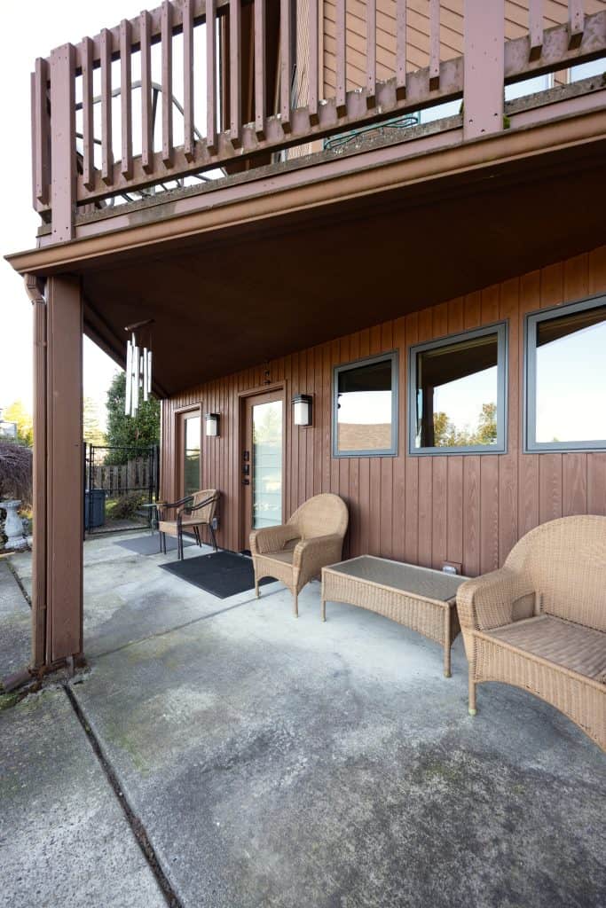 Basement patio area with wooden siding, two wicker chairs, and large windows, showcasing a remodeled outdoor space by ReCraft Home Remodeling in Portland.
