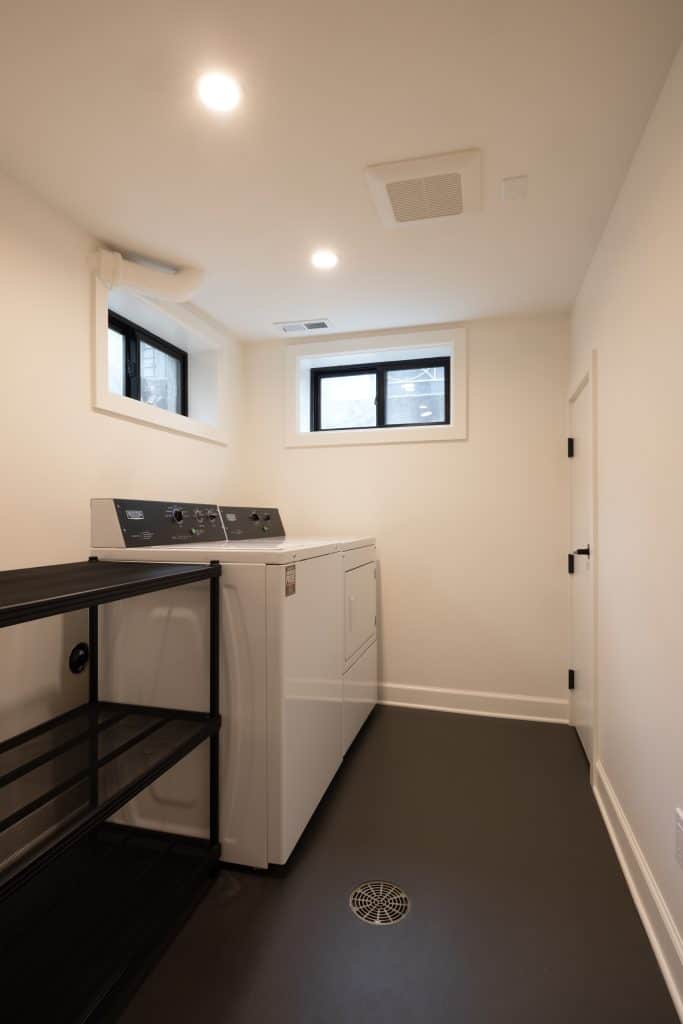 Modern basement laundry room with white appliances, black shelving unit, and natural light from windows, showcasing ReCraft Home Remodeling's renovation work in Portland.