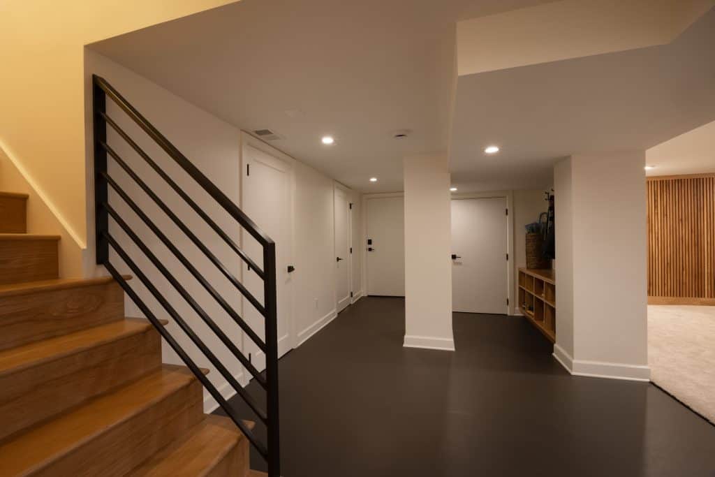 Basement hallway with modern lighting, sleek black flooring, and a staircase featuring a metal railing, showcasing a remodeled space by ReCraft Home Remodeling in Portland.