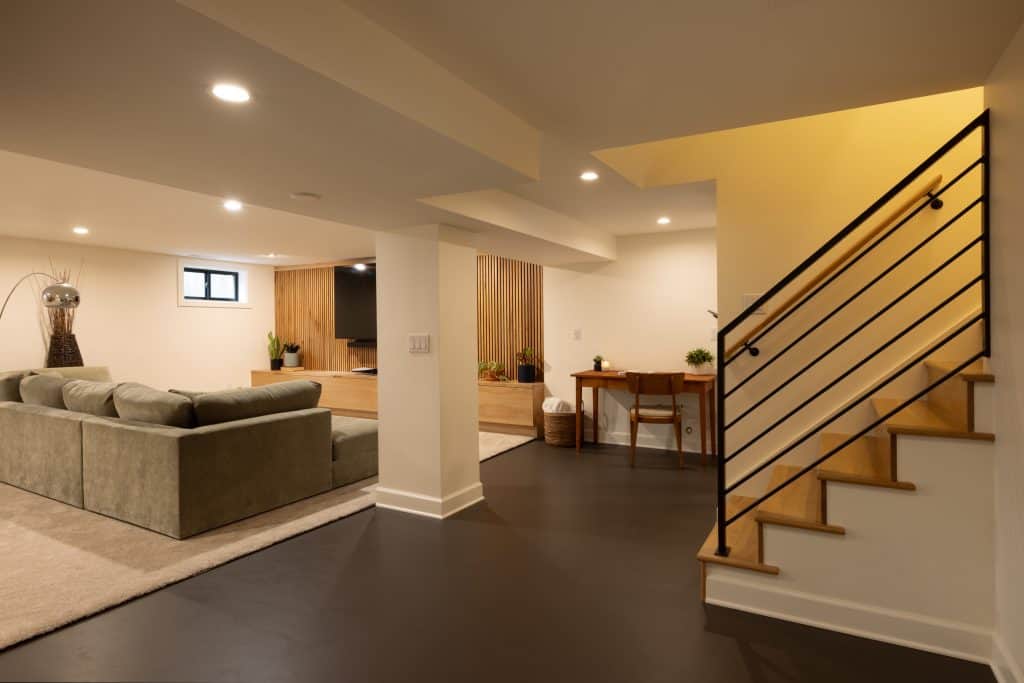 Modern basement renovation showcasing a cozy seating area with a green sofa, elegant lighting, and a staircase leading to an upper level, highlighting ReCraft Home Remodeling's design expertise in Portland.