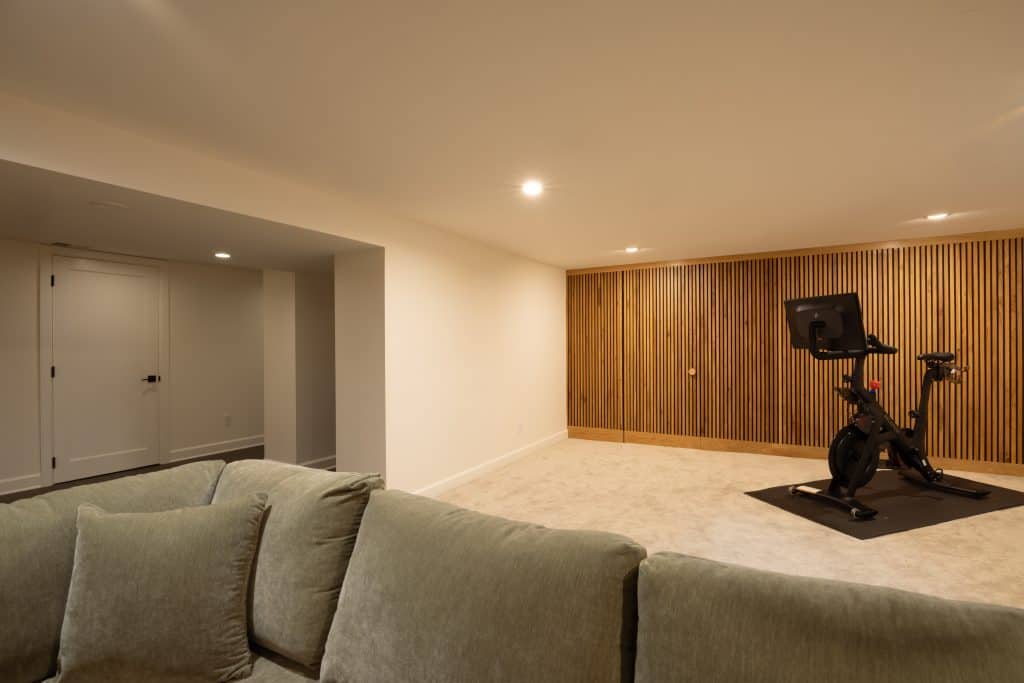 Modern basement renovation by ReCraft Home Remodeling featuring a cozy seating area and a fitness bike against a stylish wood-paneled wall in Portland, Oregon.