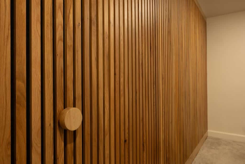 Wooden slat wall with round knob in modern basement renovation by ReCraft Home Remodeling, showcasing elegant design in Portland, Oregon.