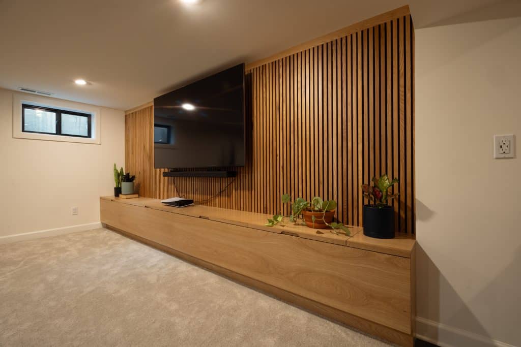Modern basement renovation featuring a wooden accent wall with a mounted television, contemporary cabinetry, and indoor plants, showcasing ReCraft Home Remodeling's design expertise in Portland.