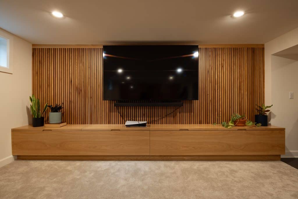 Modern basement renovation featuring a sleek wooden media console, large wall-mounted TV, and decorative plants, showcasing ReCraft Home Remodeling's design expertise in Portland.