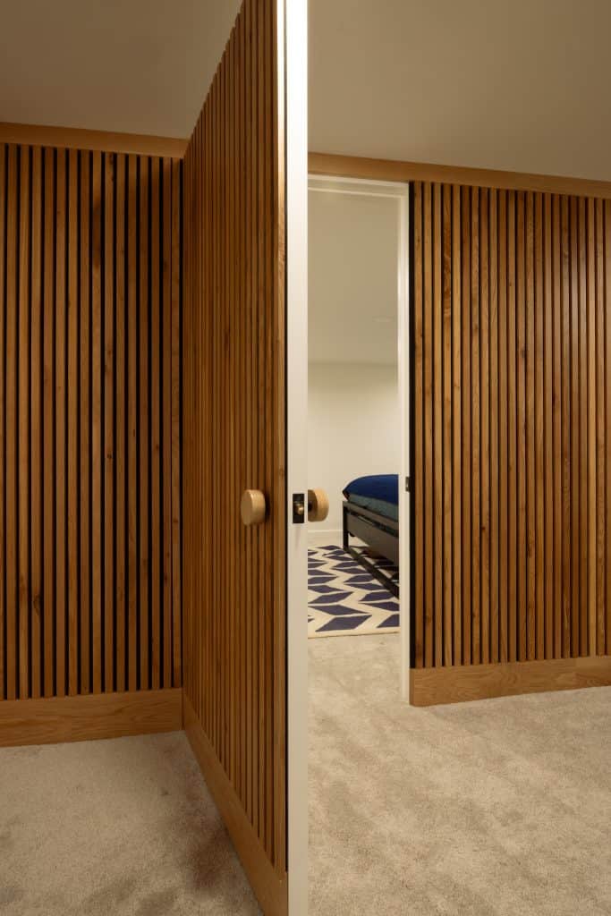 Wooden slatted doors partially open to reveal a stylishly remodeled basement bedroom with a blue bed and patterned rug, showcasing ReCraft Home Remodeling's design expertise in Portland.