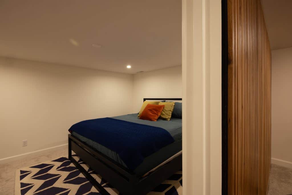 Cozy remodeled basement bedroom featuring a blue bedspread, colorful pillows, and modern decor, showcasing ReCraft Home Remodeling's design expertise in Portland.