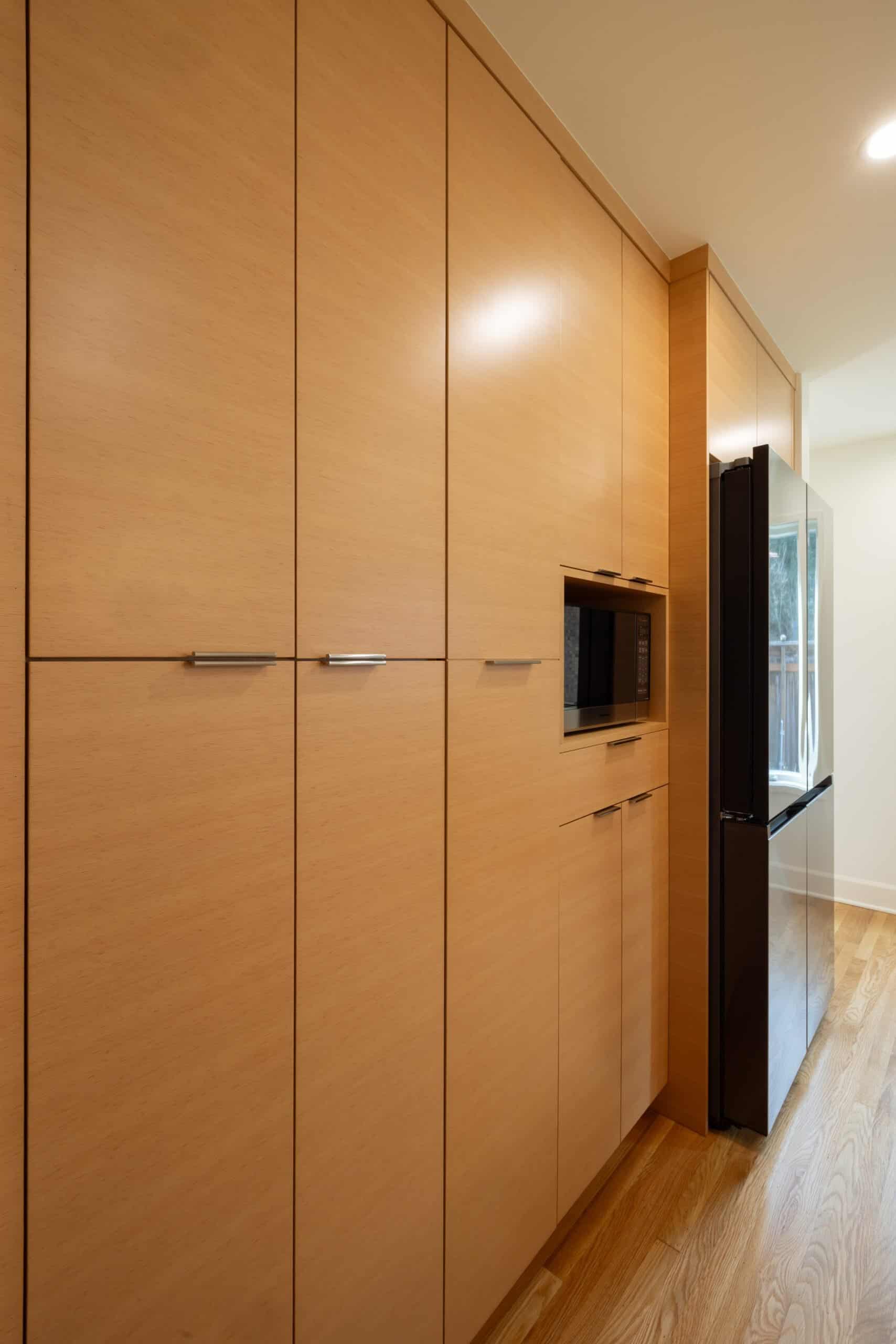 Modern kitchen with light wood cabinets, a built-in microwave, and a stainless steel refrigerator on a wooden floor.
