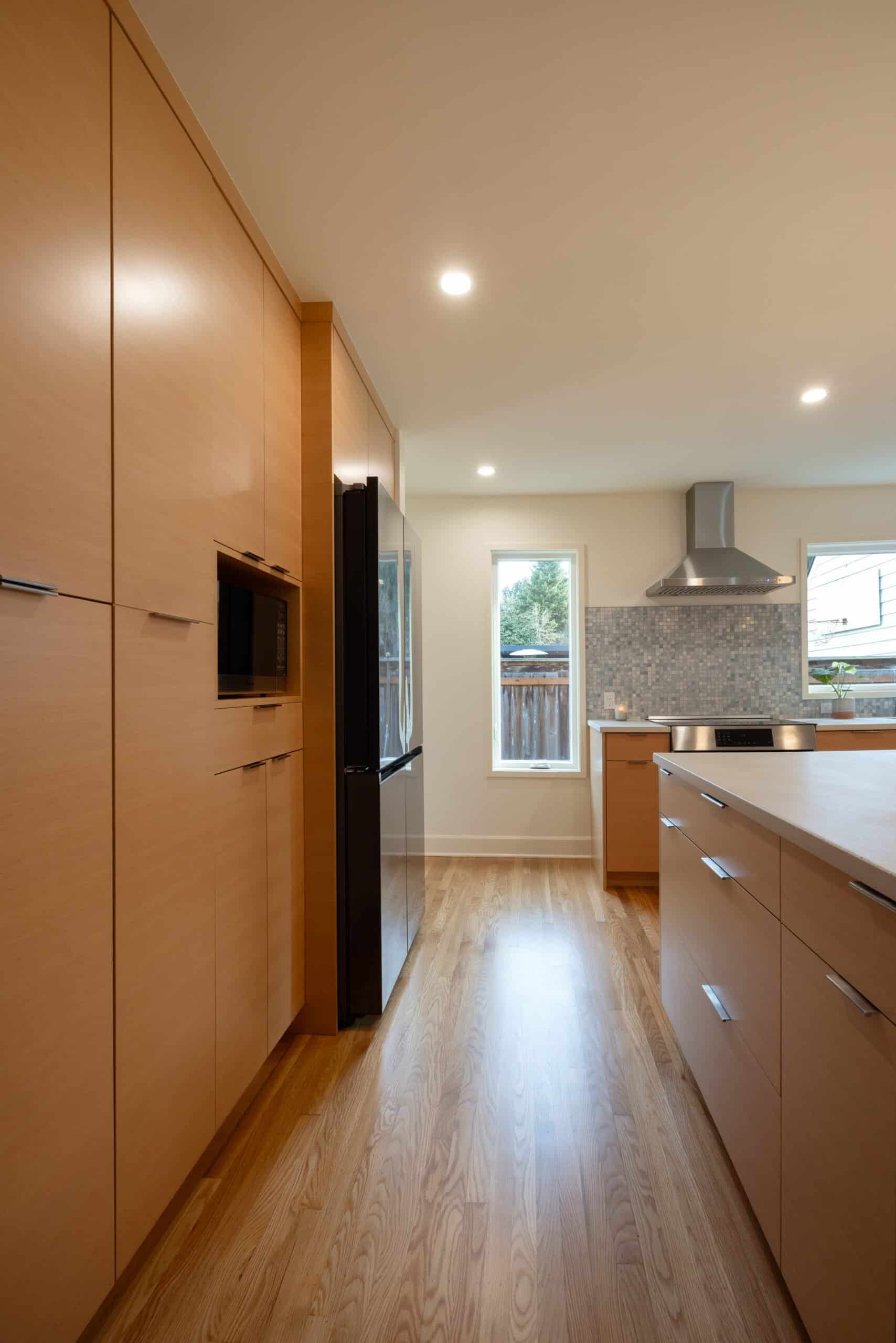 Modern kitchen with light wood cabinets, stainless steel appliances, an island counter, hardwood floors, and natural light from a window.