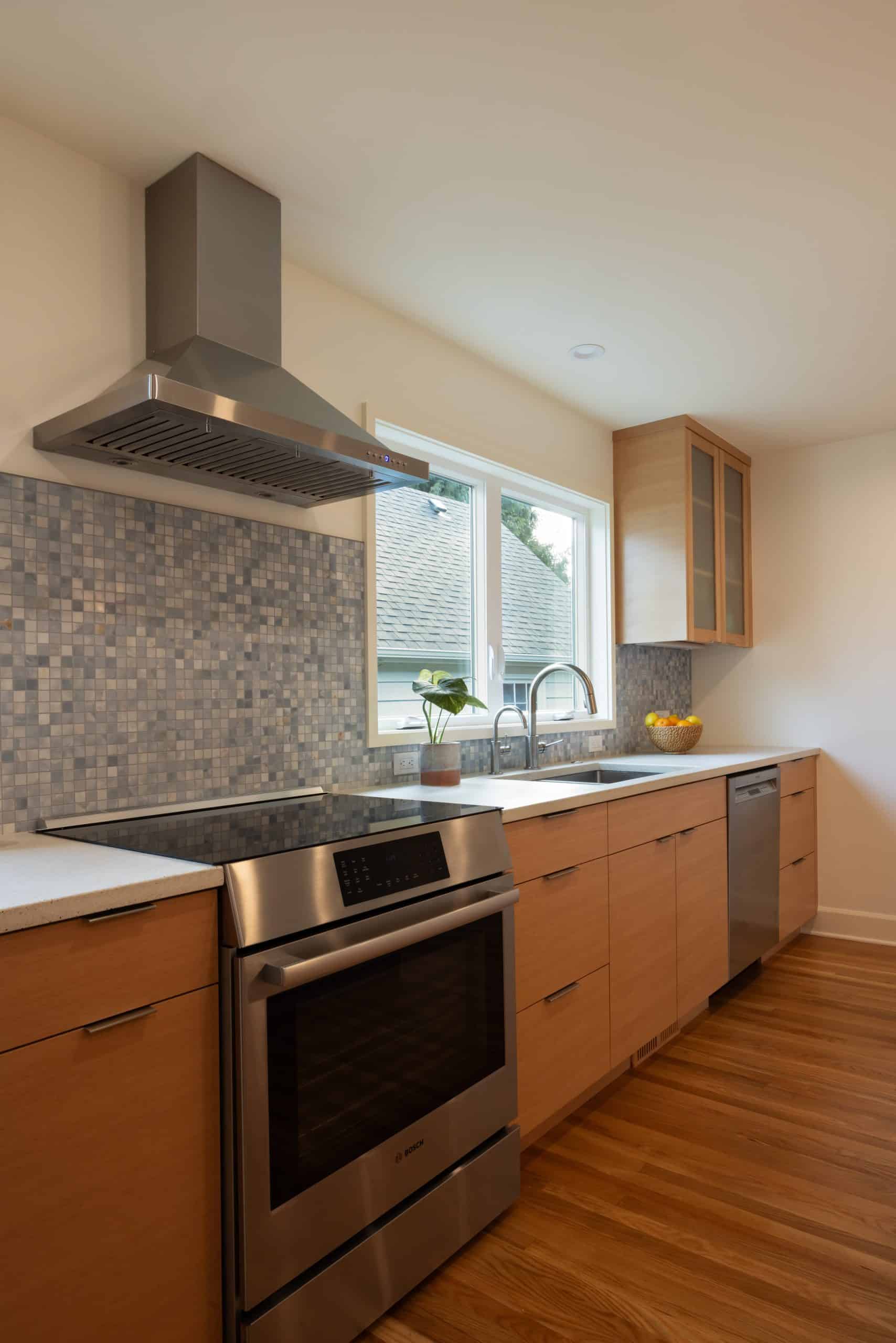 Modern kitchen with light wood cabinets, stainless steel appliances, tile backsplash, and a window above the sink letting in natural light.