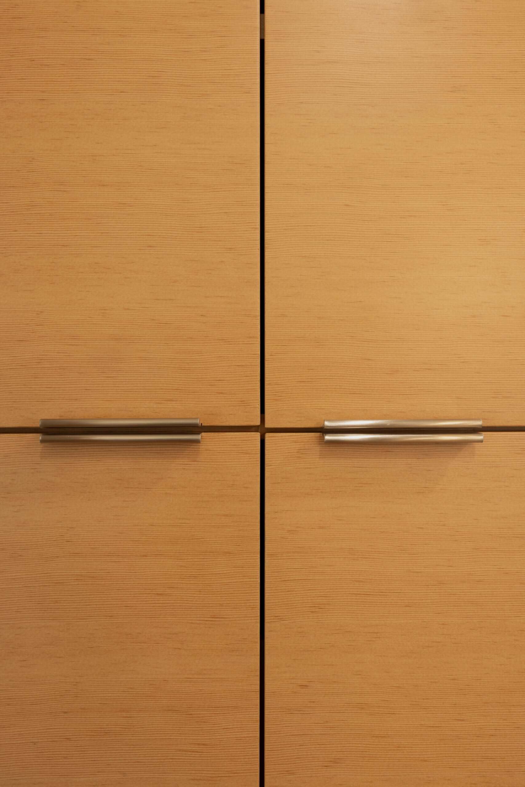 Close-up of four light wood cabinet doors with metal horizontal handles, arranged in a grid pattern.
