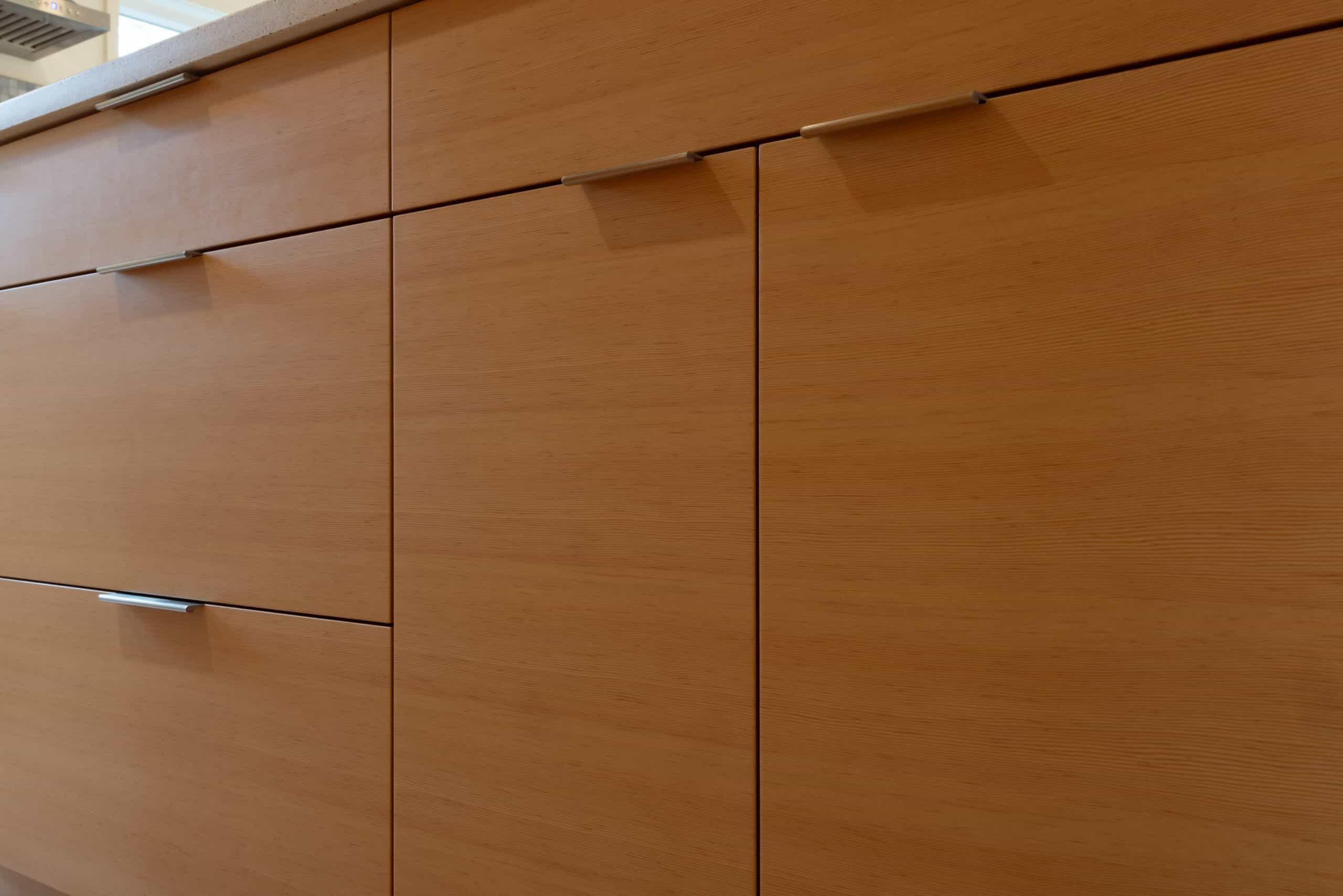 A close-up view of light wood kitchen cabinets with metal handles, aligned in a row under a light-colored countertop.