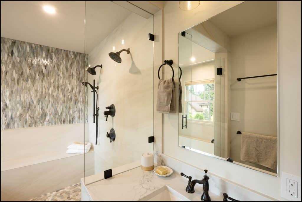 Modern bathroom with glass shower, black fixtures, a marble countertop with sink, towel rings, and a textured accent wall by the bathtub. Natural light comes through a window in this award-winning remodel of residential interior design.
