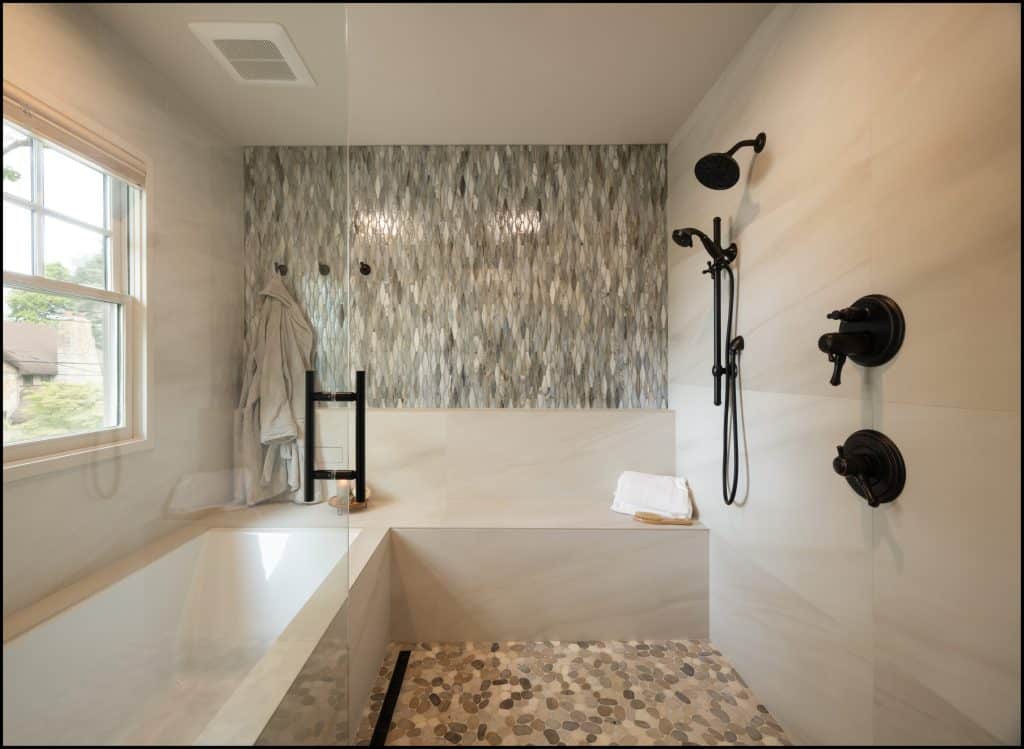 Modern bathroom by an award-winning remodeler of the year, featuring a bathtub, walk-in shower with black fixtures, mosaic tile accent wall, pebble floor, window, towel, and bathrobe on a hook.