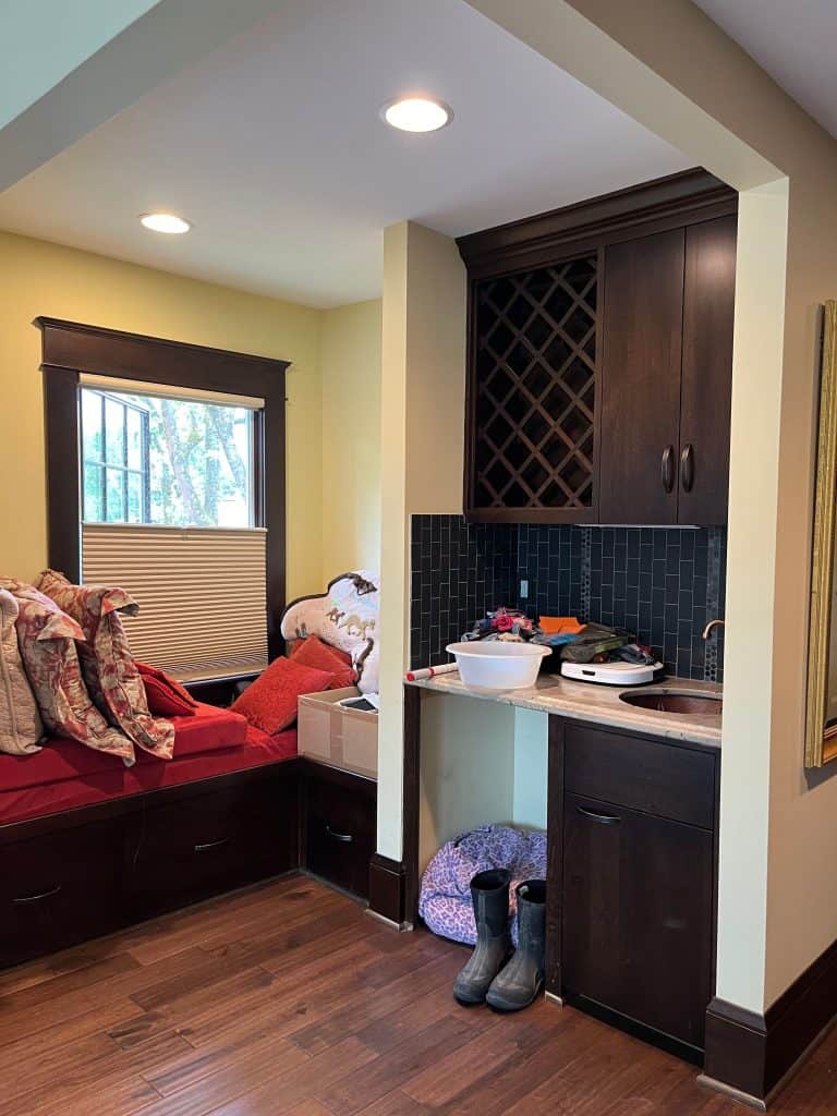 A small corner nook with a built-in bench, cushions, storage drawers, a wine rack cabinet, and a pair of boots on the floor—showcasing the refined touch of a NARI residential interior remodel.