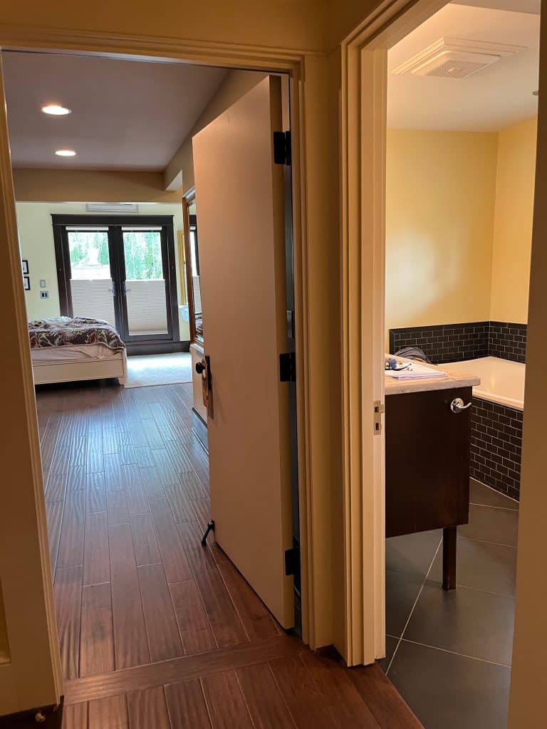 A hallway with wood flooring, part of an award-winning remodel, leads to a bedroom on the left and a bathroom with a bathtub and sink on the right.