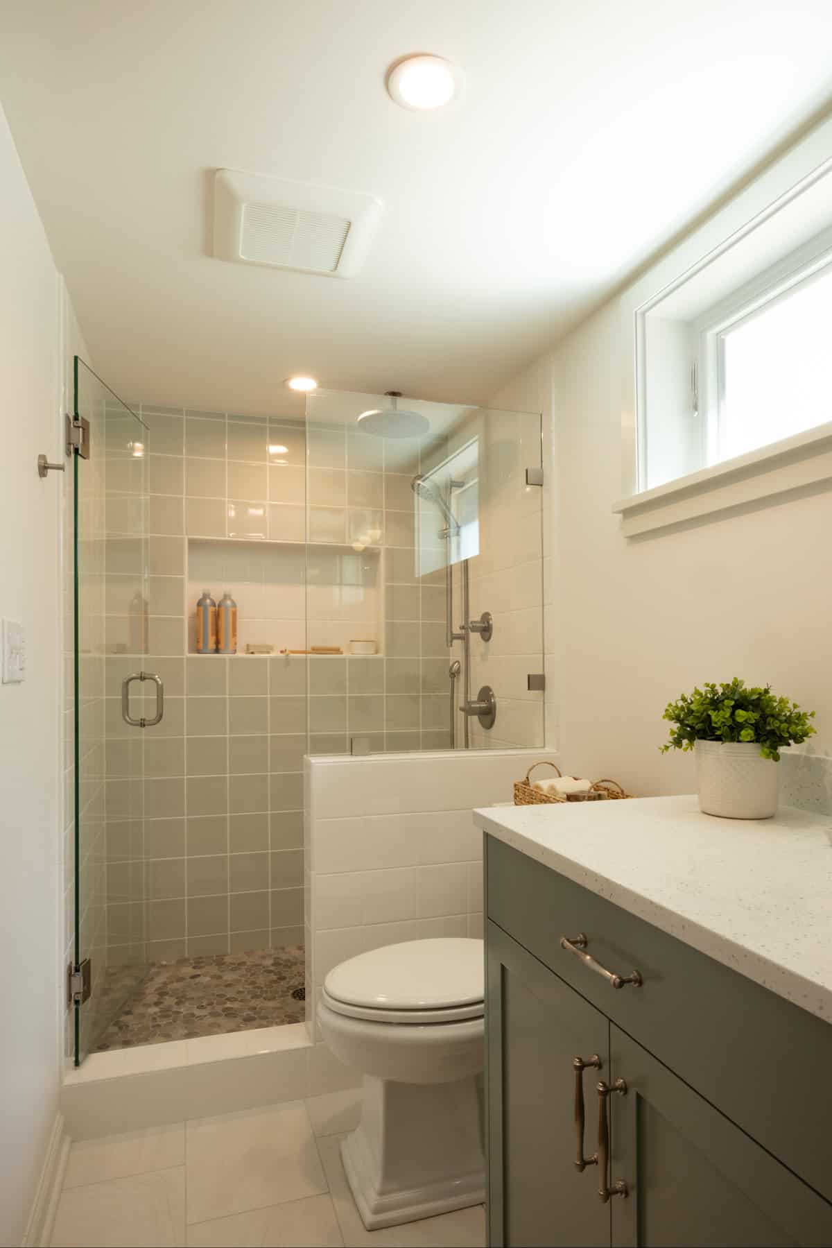 Modern bathroom with glass shower enclosure, white tile, gray vanity, countertop decor, and a small window providing natural light.